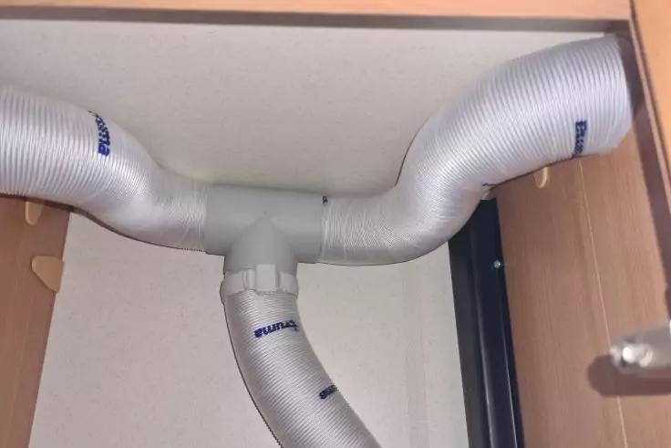 Innen eines Schranks mit drei wei&szlig;en, welligen Kunststoffschl&auml;uchen, die an einer T-f&ouml;rmigen Verbindung befestigt sind; sichtbares Holz des Schrankinneren