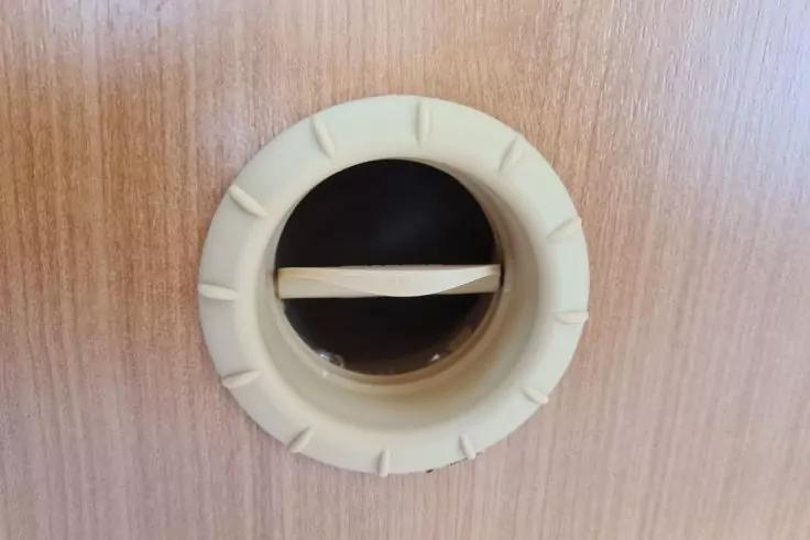 Rundes, beiges Kunststoffteil mit einer horizontalen Lamelle in einer hellen Holzplatte