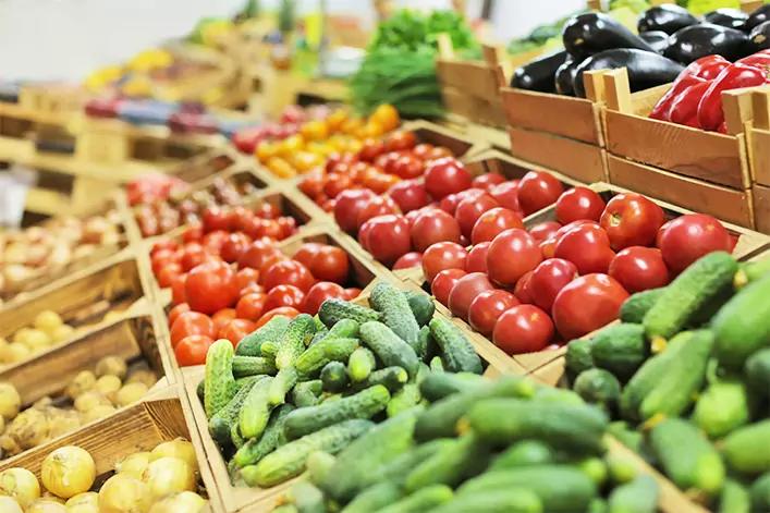 Holzkisten mit verschiedenen Gem&uuml;sen: Gurken im Vordergrund, Tomaten, Kartoffeln, Auberginen und rote Paprika, gr&uuml;ne Bl&auml;tter im Hintergrund