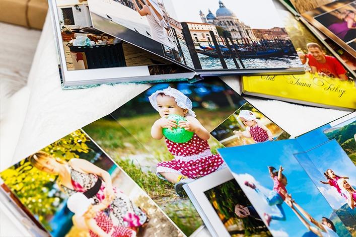 Aufgeschlagene Fotoalben und mehrere lose Fotodrucke liegen auf einer Oberfl&auml;che; sichtbar sind Kinderfotos, darunter ein Kleinkind in einem gepunkteten Kleid mit einem gr&uuml;nen Ball