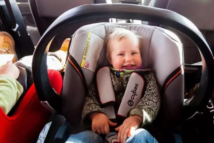 L&auml;chelndes Kind in einer Babyschale mit Trageb&uuml;gel im Auto