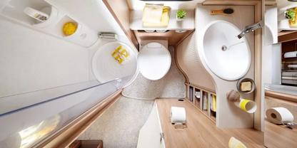 Badezimmer aus der Vogelperspektive mit Toilette, rundem Waschbecken und Wasserhahn, Duschkabine links, Holzarbeitsfl&auml;che mit Seifenspender und Becher, Toilettenpapier auf Ablage, gefaltete Handt&uuml;cher auf einem Regal, kleiner Blumentopf am Fenster