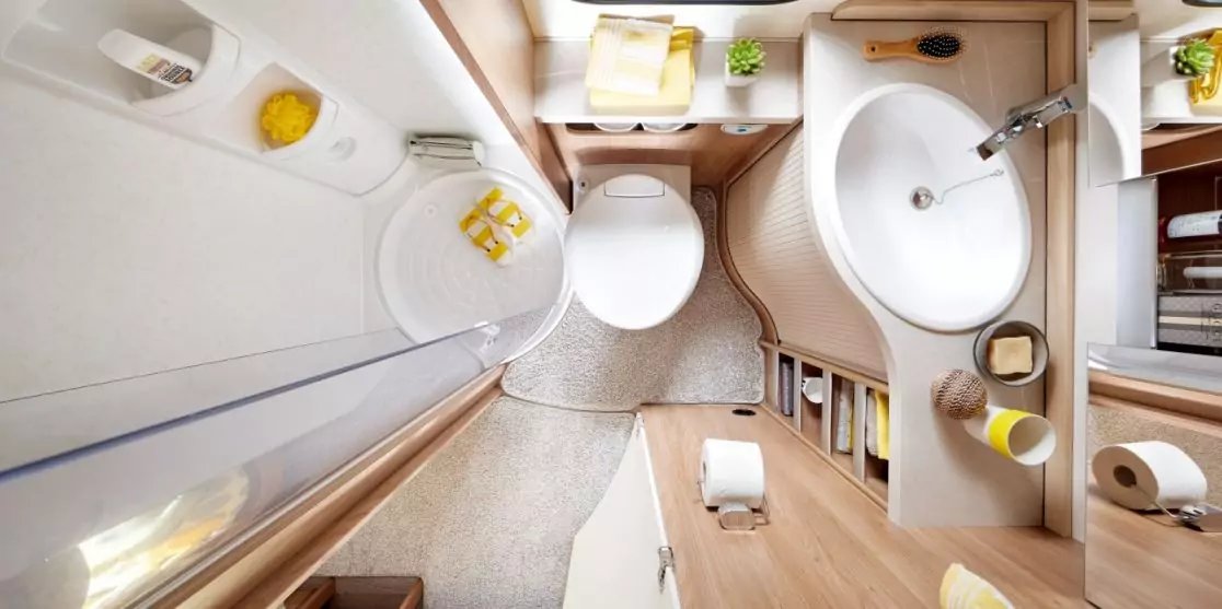 Badezimmer aus der Vogelperspektive mit Toilette, rundem Waschbecken und Wasserhahn, Duschkabine links, Holzarbeitsfl&auml;che mit Seifenspender und Becher, Toilettenpapier auf Ablage, gefaltete Handt&uuml;cher auf einem Regal, kleiner Blumentopf am Fenster