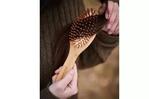 Zwei Hände halten eine Haarbürste aus Holz mit hölzernen Borsten