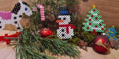 Tannenzweige auf Holzuntergrund, zwei rote Kugeln mit goldenem Muster, B&uuml;gelperlenfiguren: Einhorn, Schneemann, Tannenbaum, Tannenzapfen