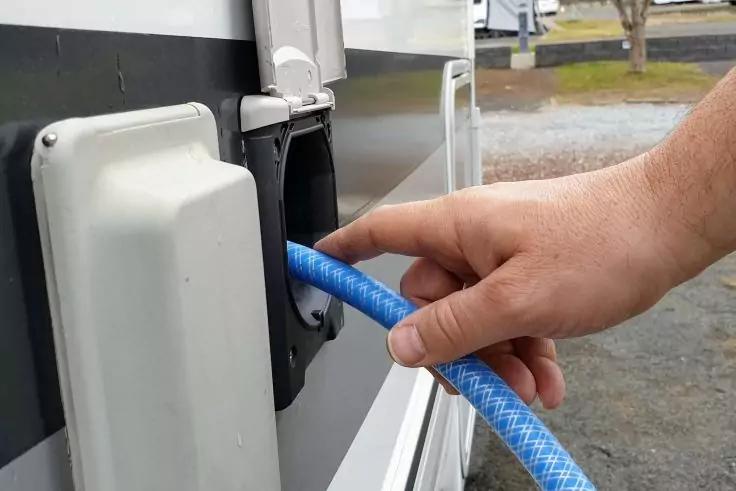 Hand steckt blauen Schlauch in Anschluss an der Seitenwand eines Fahrzeugs