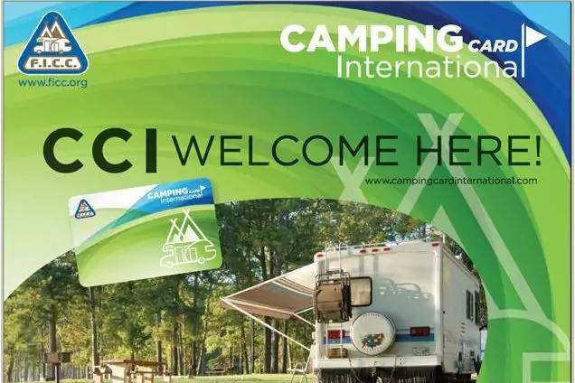 Wohnmobil mit ausgefahrener Markise steht auf Wiese vor B&auml;umen; oberer Bereich zeigt gr&uuml;nes und blaues Grafiklayout mit den Texten "CCI WELCOME HERE!" und "CAMPING card International" sowie Logos