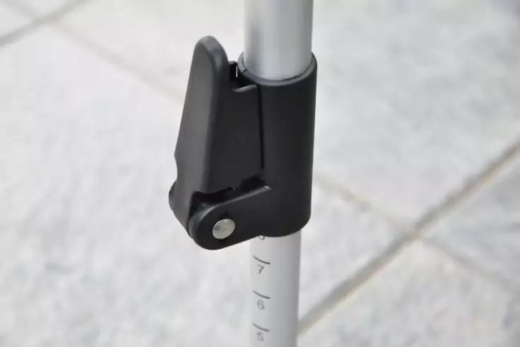 Schwarze Kunststoffklemme an silbernem Teleskoprohr mit sichtbarer Metallniete und Skalenmarkierungen, hellgraue Bodenfliesen im Hintergrund