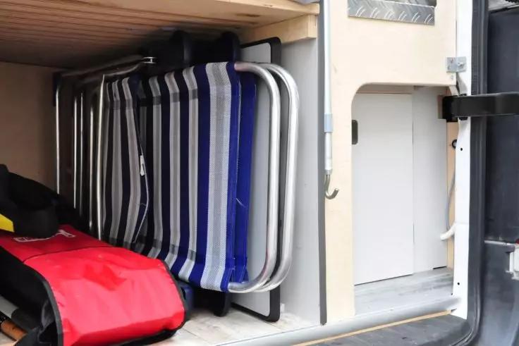 Offenes Au&szlig;enfach mit gefalteten St&uuml;hlen mit blau-wei&szlig;en Streifen, einer roten Tasche und Metallrahmen