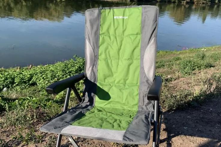 Gr&uuml;n-grauer klappbarer Campingstuhl am Ufer eines Gew&auml;ssers, im Hintergrund Wasser und Ufervegetation