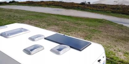 Dach eines wei&szlig;en Wohnwagens mit vier wei&szlig;en Dachluken und einem schwarzen rechteckigen Panel, im Hintergrund Gras, ein schmaler Wassergraben und sandige D&uuml;nen