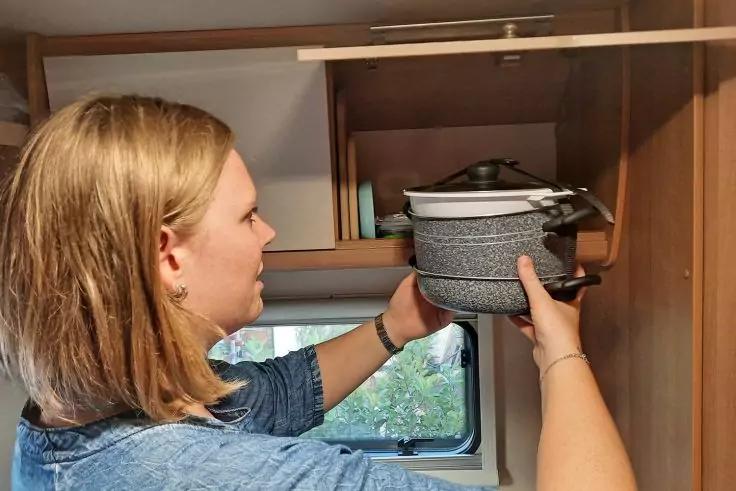 Person legt einen Topf mit Deckel in ein oberes Holzfach &uuml;ber einem Fenster