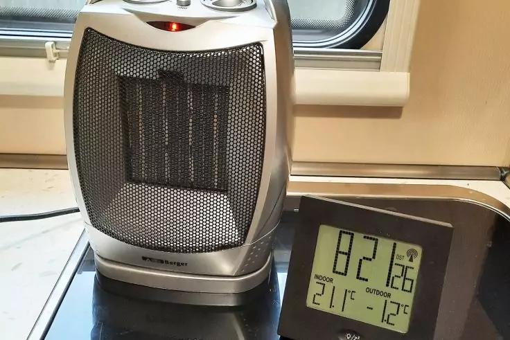 Silberner tragbarer Heizl&uuml;fter auf einer Arbeitsfl&auml;che vor einem Fenster; rechts digitales Thermometer zeigt 22.1&deg;C