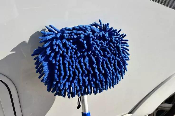 Blaues Mikrofasertuch mit vielen Fransen an einem Stiel auf der wei&szlig;en Karosserie eines Autos