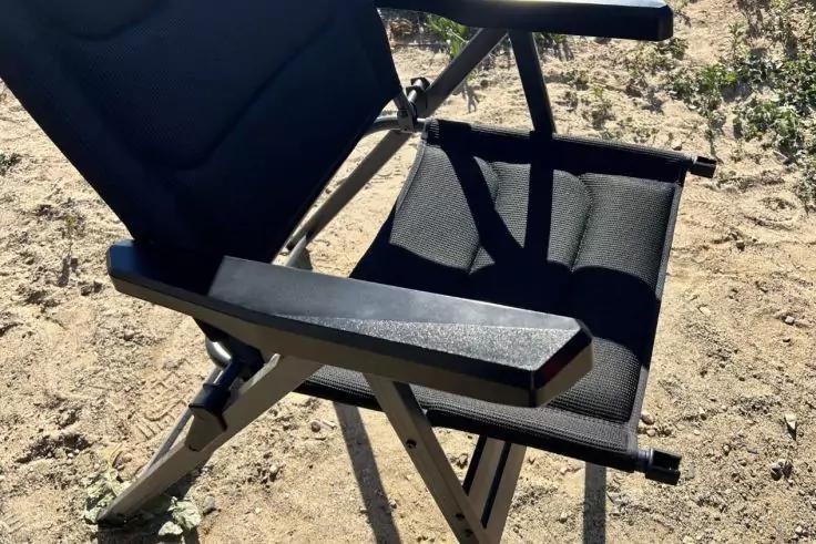 Schwarzer Klappstuhl mit Metallrahmen auf sandigem Boden, Teilansicht