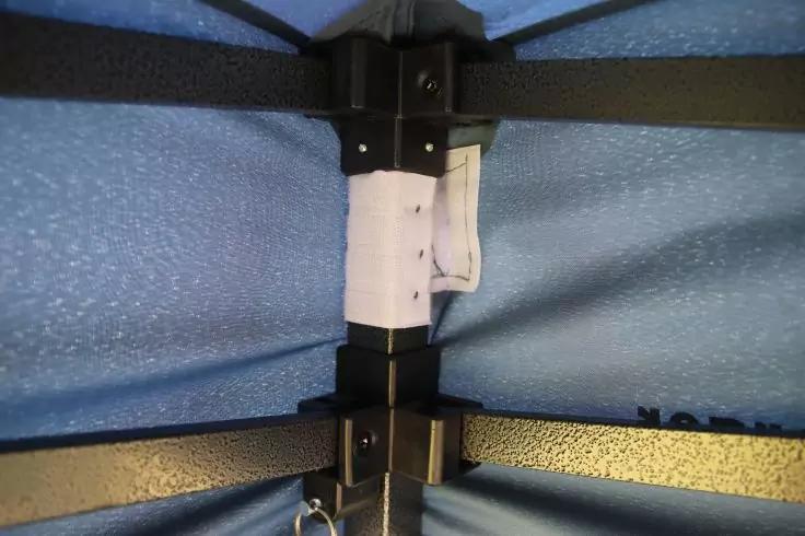 Schwarze Metallstreben kreuzen sich an einem zentralen Verbindungspunkt, blaue strukturierte Stoffbespannung, wei&szlig;er Bandstreifen um den Mittelpfosten, kleiner Metallring unten