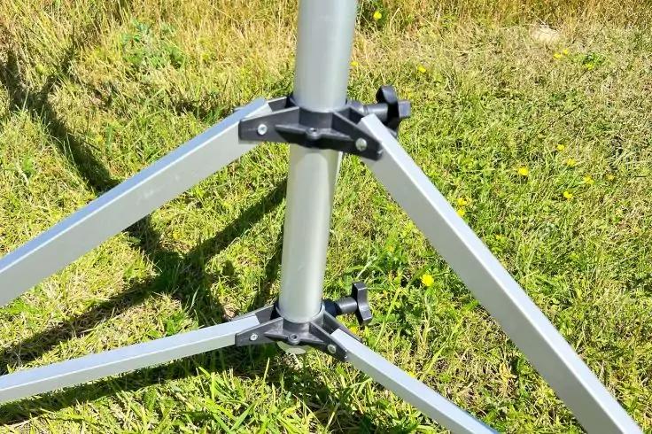 Nahaufnahme der Metallbeine eines Dreibeinstativs auf grünem Gras