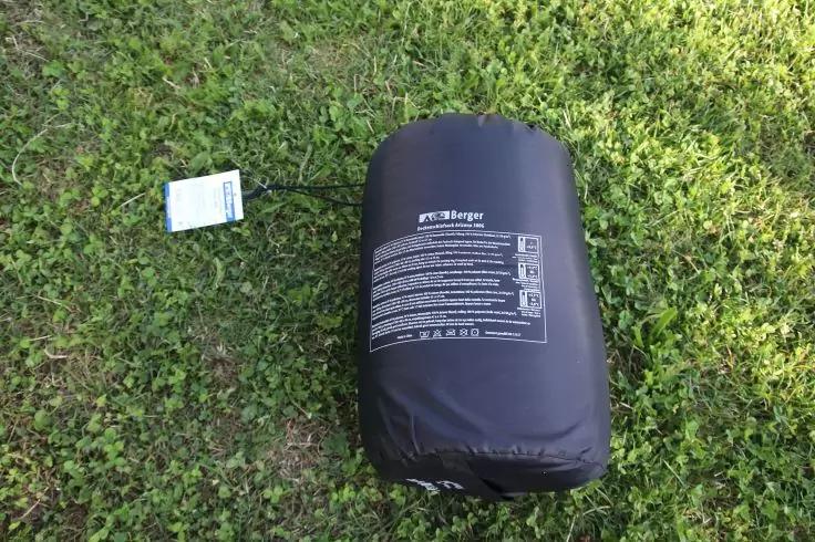 Schwarzer Packsack mit aufgedrucktem Text und wei&szlig;em Anh&auml;nger an einer Schnur, liegt auf Gras