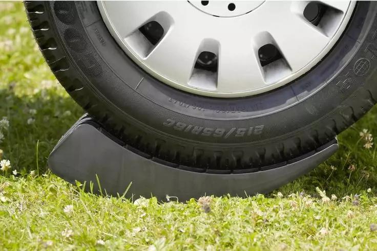 Nahaufnahme eines Reifens mit Radkappe auf einem schwarzen Auffahrkeil auf gr&uuml;nem Gras