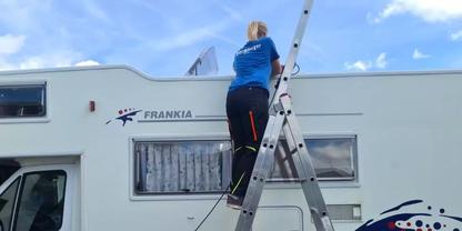 Person steht auf einer Anlegeleiter am Dach eines wei&szlig;en Wohnmobils mit der Aufschrift "FRANKIA", blauer Himmel im Hintergrund