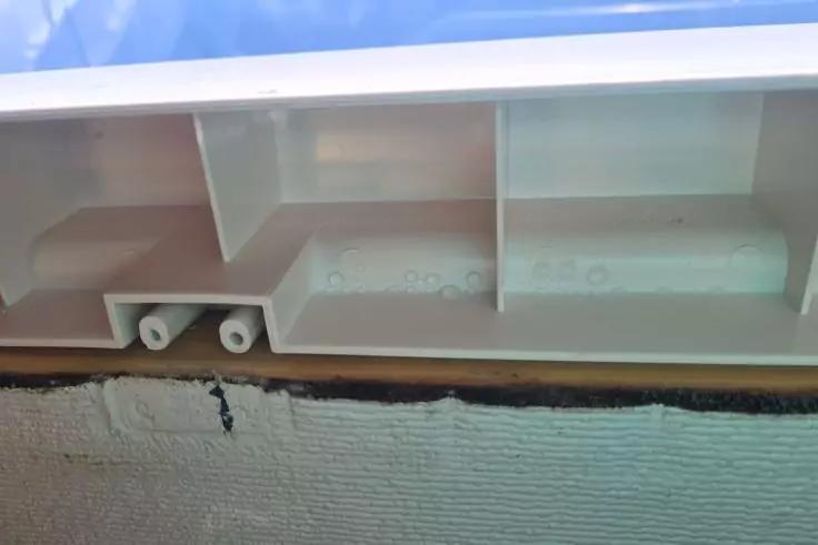 Wei&szlig;e Kunststoffleiste mit mehreren F&auml;chern; in einem Fach liegen zwei kleine wei&szlig;e Zylinder; darunter eine raue wei&szlig;e Wand mit schmaler schwarzer Fuge und braunem Streifen