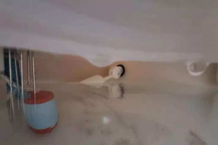 Heller Badewannenboden mit Abfluss und wei&szlig;em Stopfen, links ein rot-blauer Plastikbeh&auml;lter