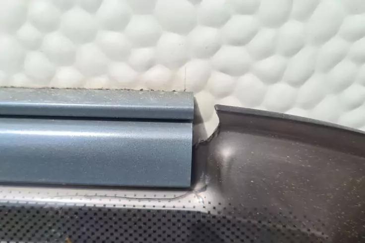 Nahaufnahme zweier aneinanderstoßender Leisten: links flache blaue Leiste, rechts gebogene schwarze Leiste mit kleinem Spalt dazwischen; im Hintergrund weiße, gewölbte wabenartige Oberfläche; unten dunkle, perforierte Fläche