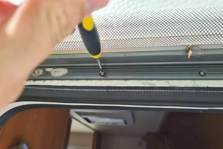 Hand mit Schraubendreher an Schraube in dunkler Schiene über Türöffnung; Holzinnenraum im Hintergrund