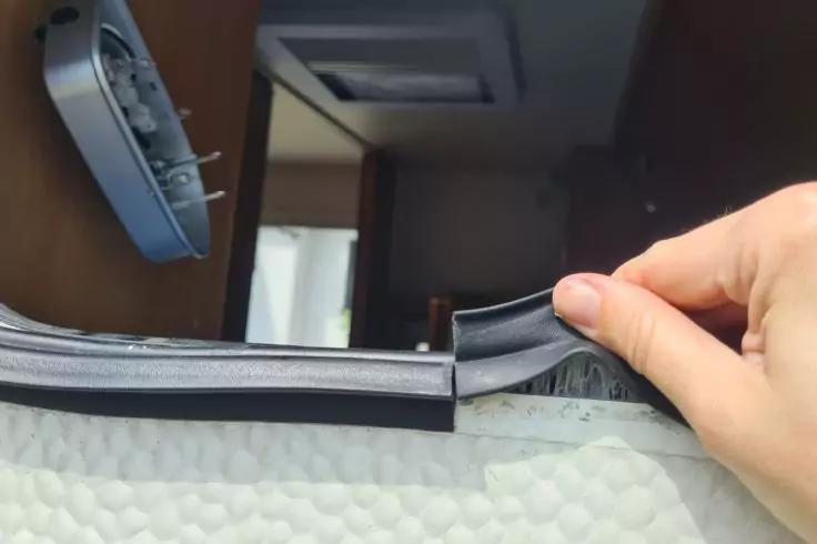 Hand zieht schwarzen Reißverschluss/Bündchen zurück, darunter weißes Material mit Blasenstruktur; links Wandsteckdose mit eingestecktem Adapter, im Hintergrund Türöffnung und Deckenlüftung