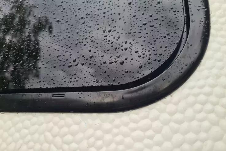 Fensterscheibe mit Regentropfen, schwarze Dichtung, weiße strukturierte Oberfläche