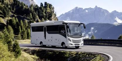 Wei&szlig;es Wohnmobil auf einer kurvigen Bergstra&szlig;e, links B&auml;ume, im Hintergrund schneebedeckte Berge