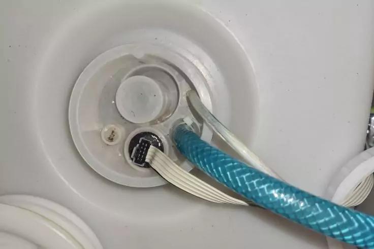 Rundes wei&szlig;es Kunststoffteil mit drei &Ouml;ffnungen, blauem geflochtenem Schlauch, klarem Schlauch und wei&szlig;em mehradrigem Flachkabel auf wei&szlig;er Oberfl&auml;che