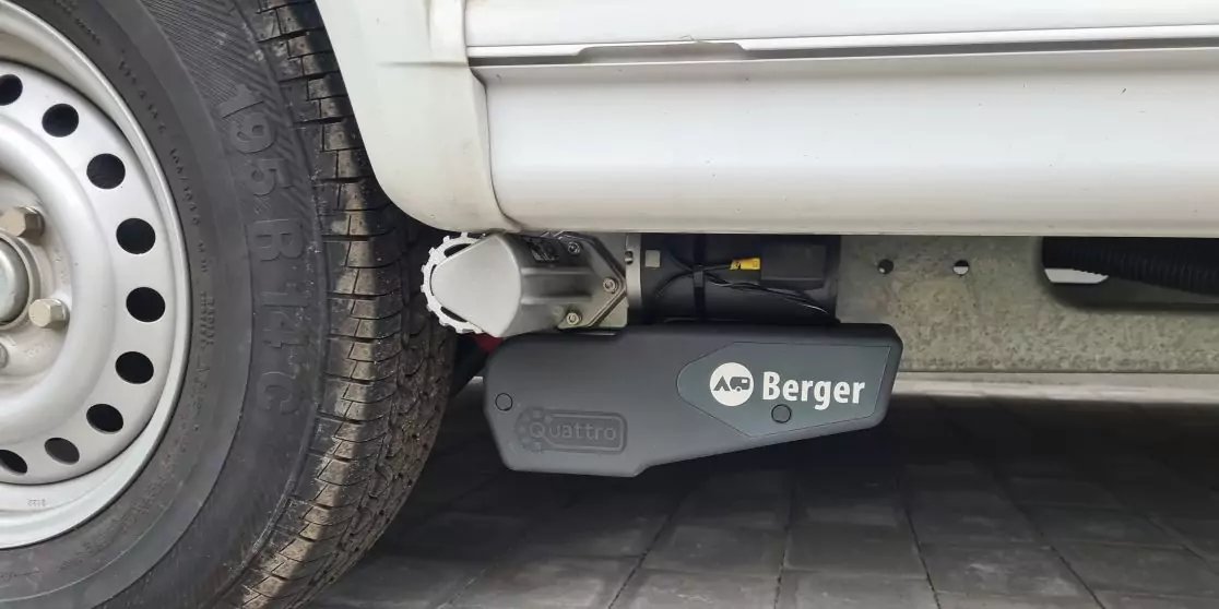 Linkes Rad eines wei&szlig;en Fahrzeugs mit Stahlfelge und Radkasten; darunter ein schwarzes Ger&auml;t mit Aufschrift "Berger"; gepflasterter Boden