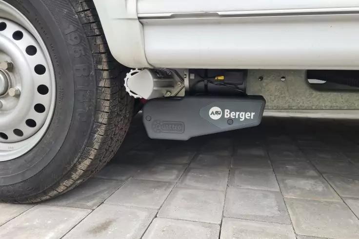 Linkes Rad eines weißen Fahrzeugs, darunter ein schwarzes Gerät mit weißer Aufschrift Berger, daneben ein weißes zylindrisches Bauteil, grauer Unterboden und Pflastersteine