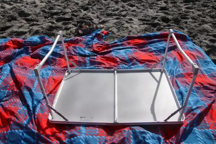 Umgedrehter kleiner Klapptisch mit Metallbeinen auf einer rot-blau gemusterten Decke auf Sand
