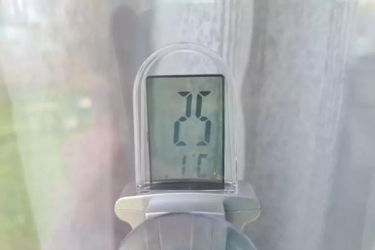 Kleines Ger&auml;t mit digitalem Display, zeigt die Ziffern '25', befestigt mit Saugnapf an einer Fensterscheibe; halbtransparenter Vorhang im Hintergrund