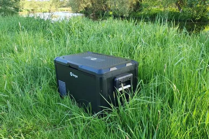 Schwarzer rechteckiger Kasten mit Griffen im hohen Gras neben einer Wasserfl&auml;che