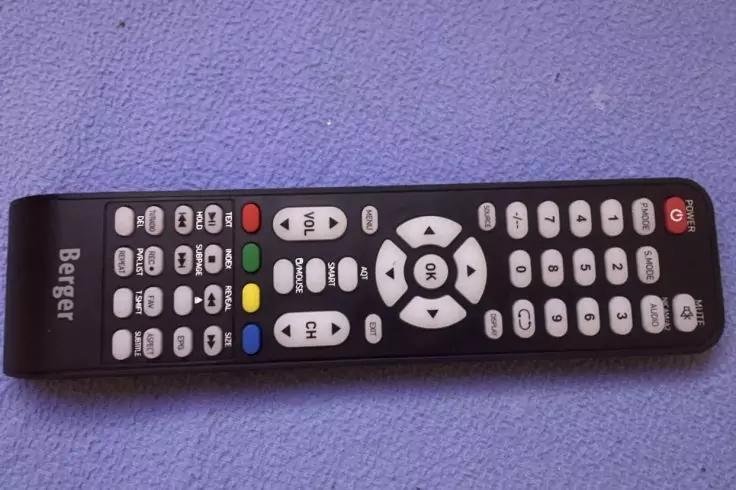 Schwarze Fernbedienung mit vielen wei&szlig;en und farbigen Tasten (rot, gr&uuml;n, gelb, blau), Schriftzug Bester links, liegend auf violettem Stoff