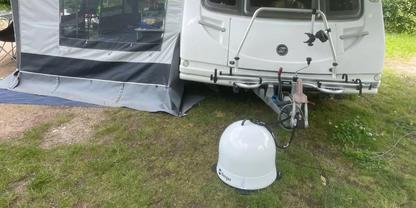 Wei&szlig;er Wohnwagen mit angebautem Vorzelt auf Gras; ein wei&szlig;er Helm liegt vor der Anh&auml;ngerkupplung