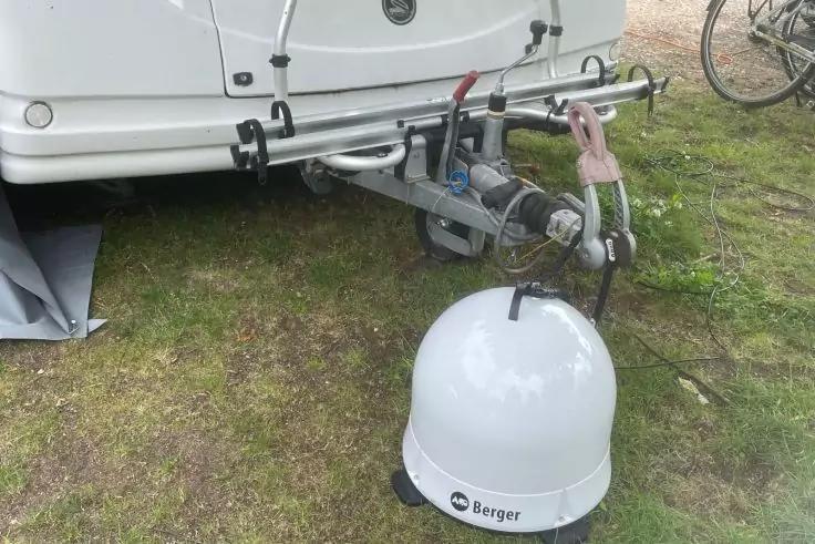 Wei&szlig;e runde Kuppel mit Aufdruck "berger" vor der Anh&auml;ngerkupplung eines wei&szlig;en Wohnwagens auf Gras; Fahrradreifen und grauer Bodenbelag sichtbar