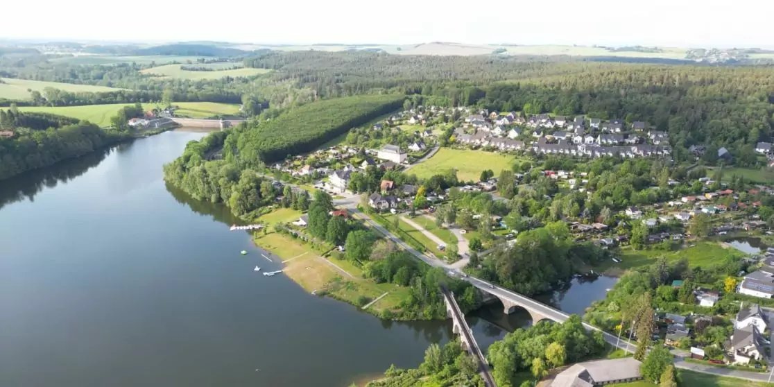 Luftaufnahme: Wasserfl&auml;che mit Ufer und Bogenbr&uuml;cke, angrenzende H&auml;user und Stra&szlig;en, B&auml;ume, Felder und Wald