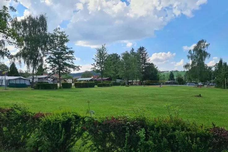 Gro&szlig;e gr&uuml;ne Rasenfl&auml;che mit niedriger Hecke im Vordergrund, B&auml;ume und kleine Geb&auml;ude/Pavillons am Rand, blauer Himmel mit Wolken