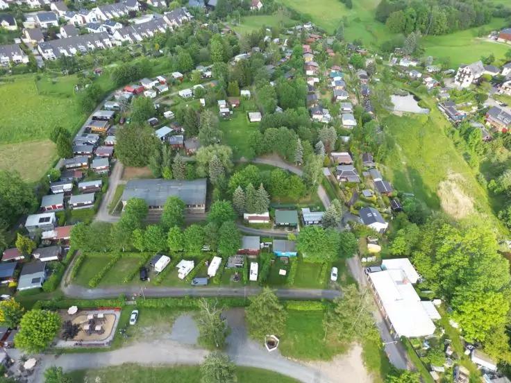 Luftaufnahme mit Reihen kleiner Geb&auml;ude und Wohnwagen, gr&uuml;nen Rasenfl&auml;chen, B&auml;umen, Wegen, Parkpl&auml;tzen und einem wei&szlig;en Geb&auml;ude rechts