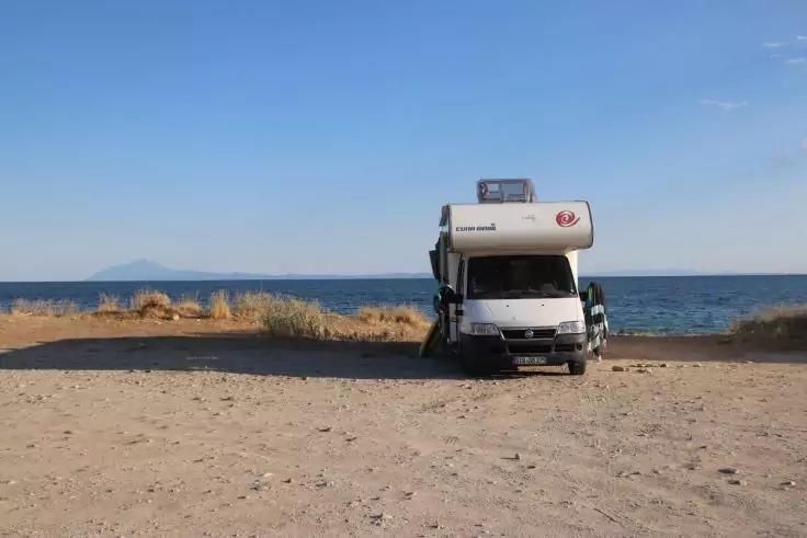 Weißes Wohnmobil auf sandiger Küste, dahinter Meer, niedrige Vegetation und blauer Himmel