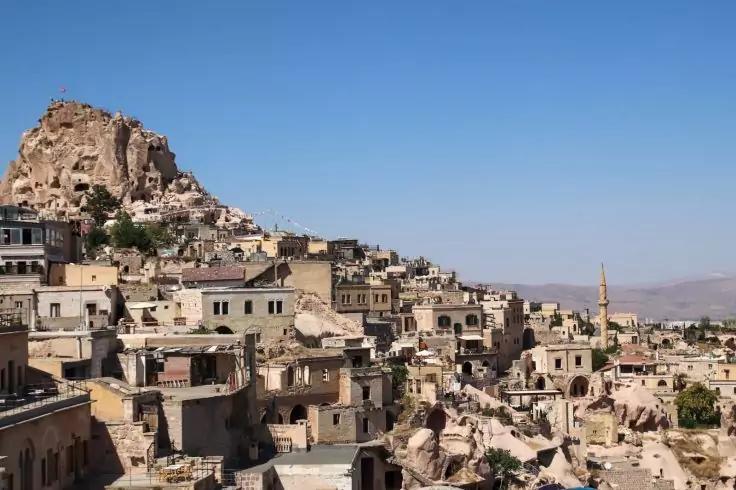 Steinbauten und H&ouml;hlenwohnungen an einer Felsflanke, hohe Felsformation mit H&auml;usern, sichtbare Minarettspitze, blauer Himmel