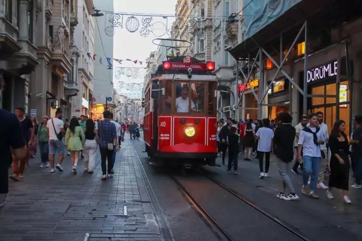 Rote Stra&szlig;enbahn auf Schienen in der Mitte einer belebten Fu&szlig;g&auml;ngerstra&szlig;e, Menschen gehen beidseits, Schaufenster und Lichterketten &uuml;ber der Stra&szlig;e