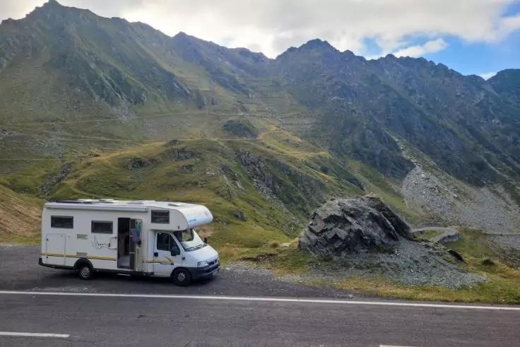 Wei&szlig;es Wohnmobil am Stra&szlig;enrand vor einer bergigen Landschaft mit Felsen und wolkigem Himmel