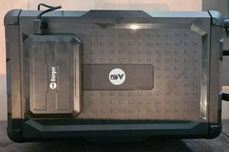 Schwarze, flache rechteckige Box mit strukturierter Oberfl&auml;che, mittig wei&szlig;es rundes Logo mit zwei dunklen Buchstaben; links aufgesetztes kleines schwarzes Ger&auml;t mit wei&szlig;er Aufschrift 'Berger' und angeschlossenem Kabel