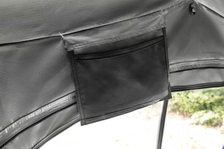 Graue Stoffbespannung mit angenähter rechteckiger Tasche, sichtbaren Nähten, Metallstange und unscharfem Außenbereich