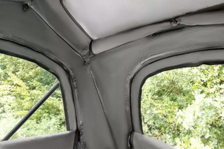 Innenraum eines Autos: graue, gepolsterte Dachverkleidung mit Nähten und Fensterrahmen; draußen grünes Laub